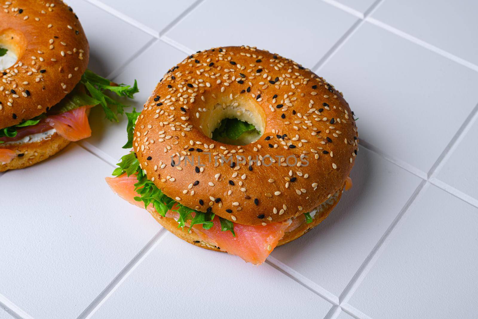 Cream cheese and smoked salmon bagel set, on white ceramic squared tile table background, with copy space for text