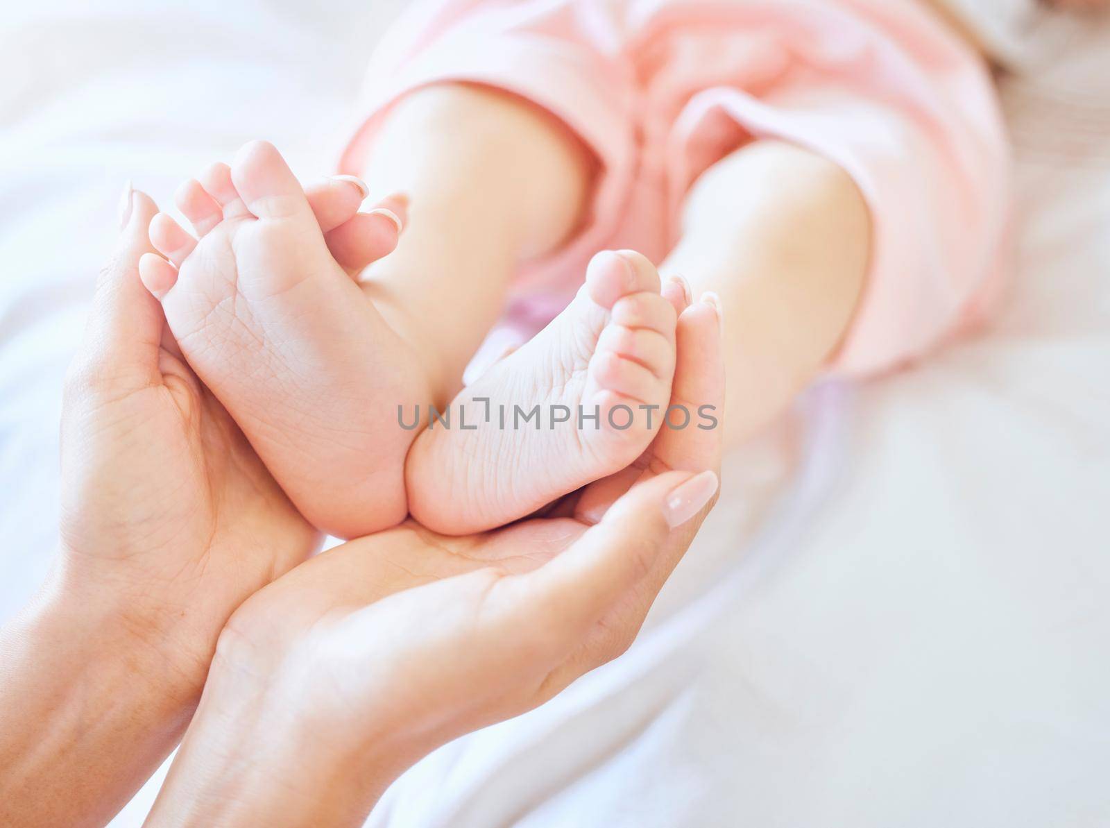 Mother holding baby feet. Closeup of tiny newborn baby feet held by a parent. Small baby toes. Little baby lying on a bed. Woman holding feet of little baby girl. Innocent infant being held by mother.