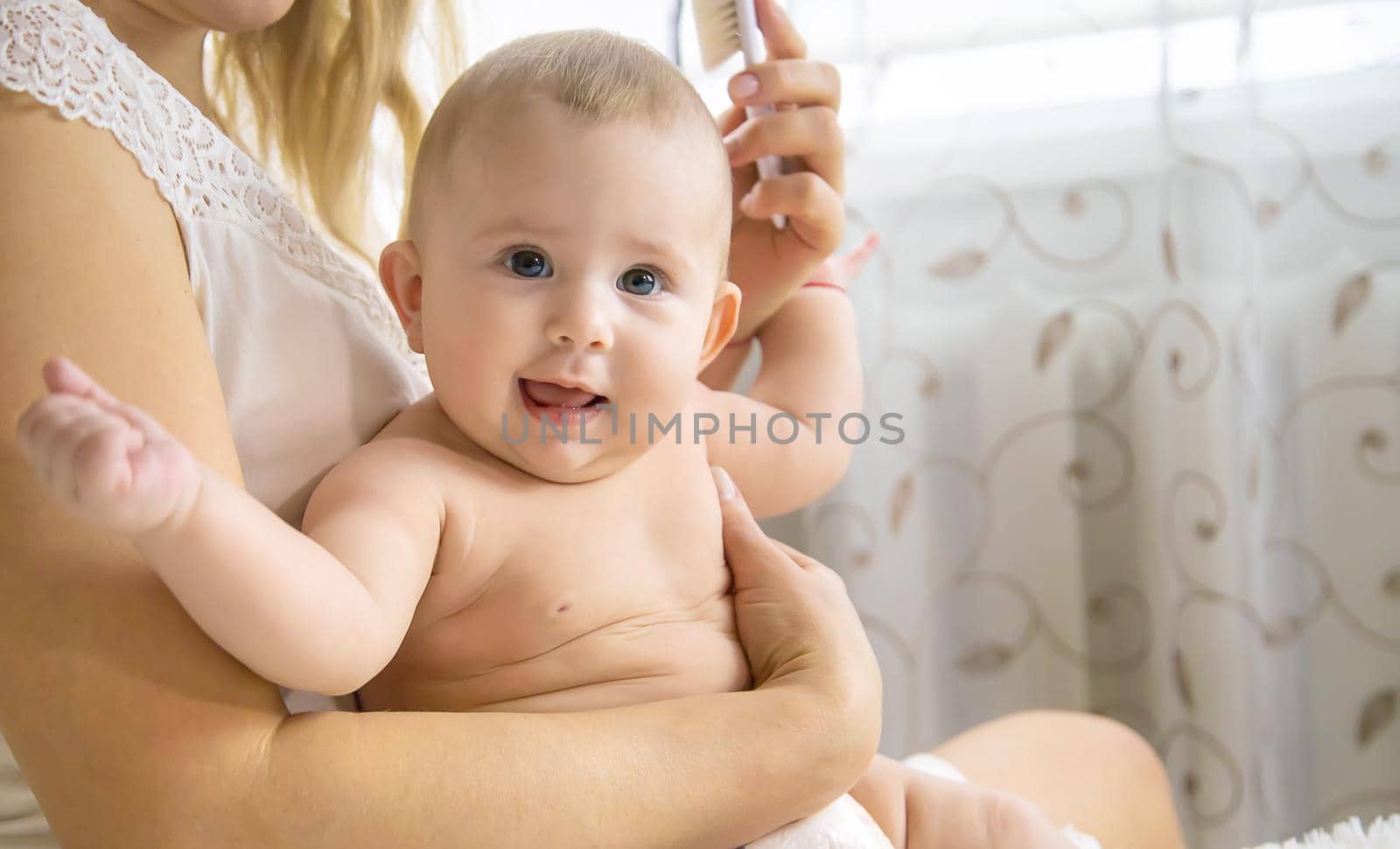 The mother is combing the little baby's hair. Selective focus. People.