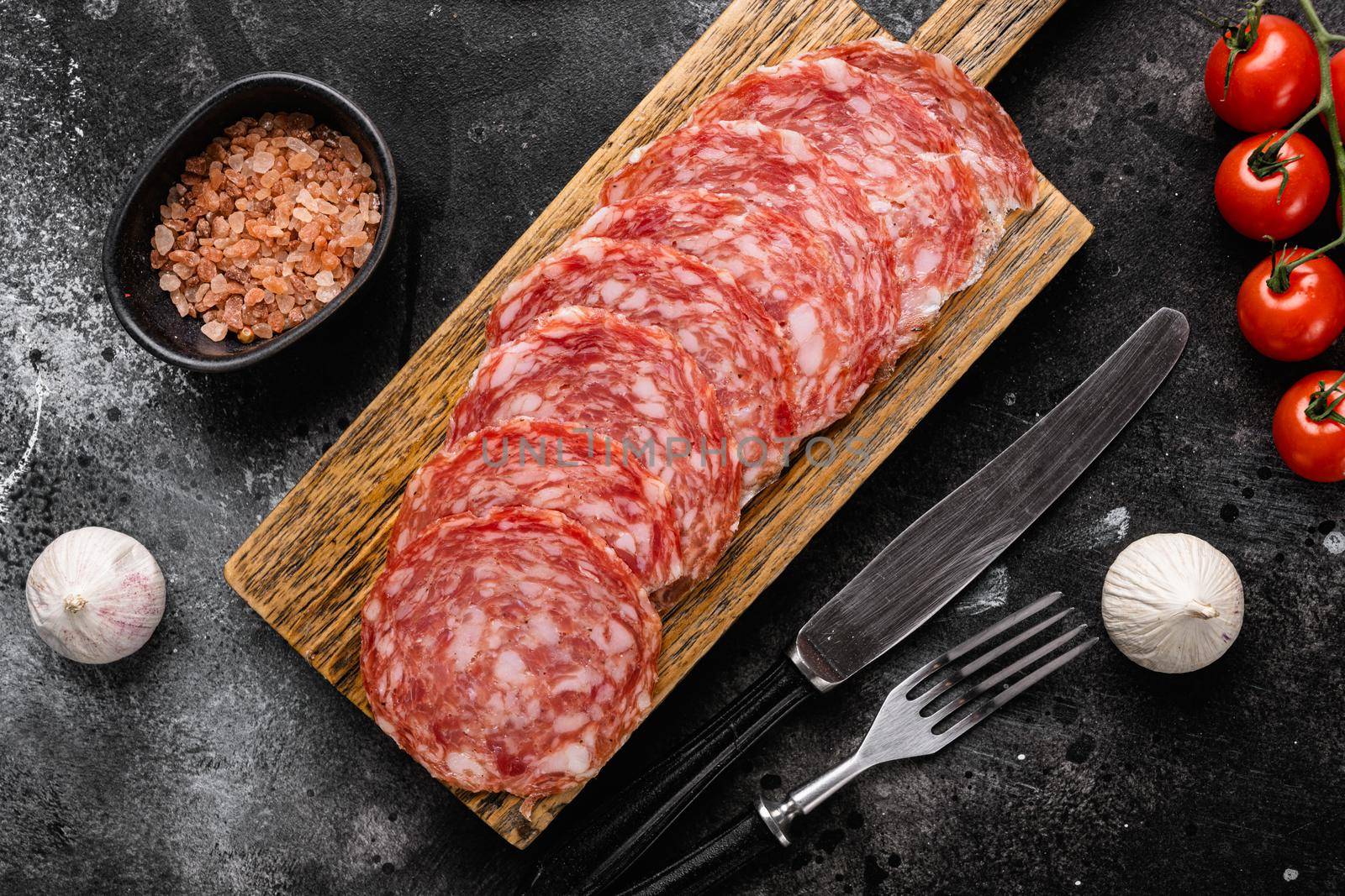 Thinly Sliced Milano salami, on black dark stone table background, top view flat lay by Ilianesolenyi