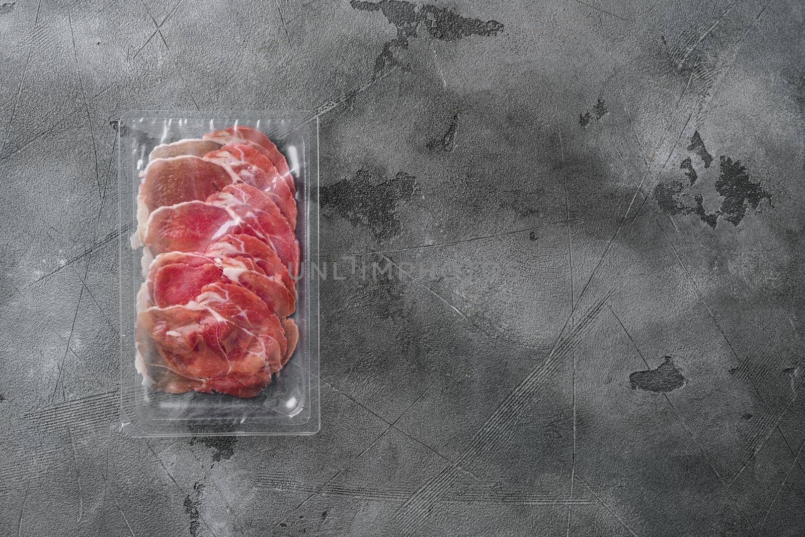 Prosciutto slices in transparent vacuum plastic pack, on gray stone table background, top view flat lay, with copy space for text by Ilianesolenyi