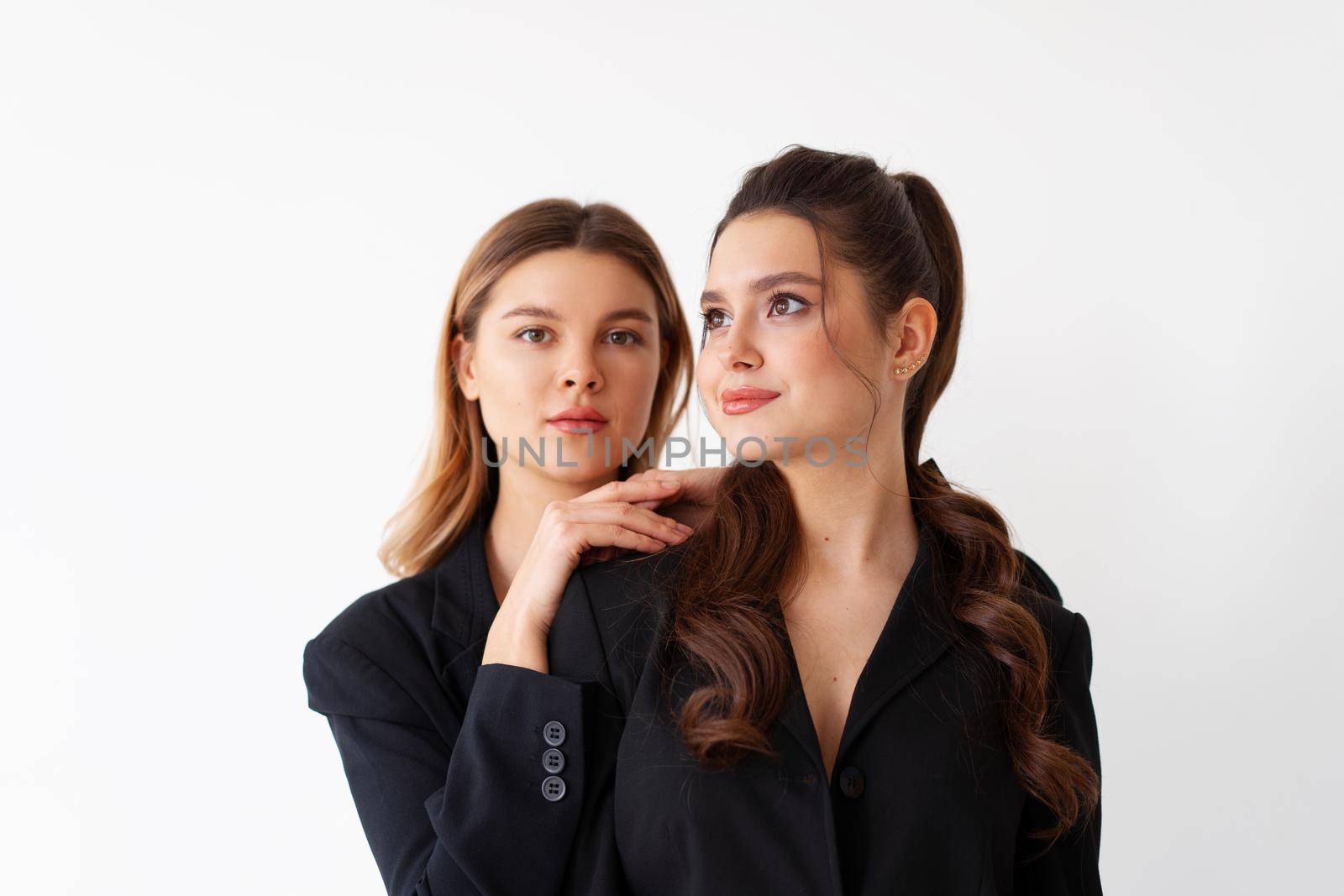 Concept of partnership in business. Two Young businesswoman dressed black formal suit standing studio isolated white background. Blonde woman put her hands on the shoulders of her friend.