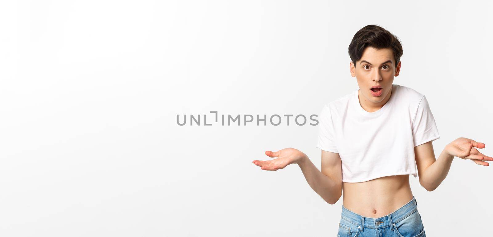 Lgbtq community. Confused gay man in crop top shrugging and staring at camera, cant understand, standing over white background.