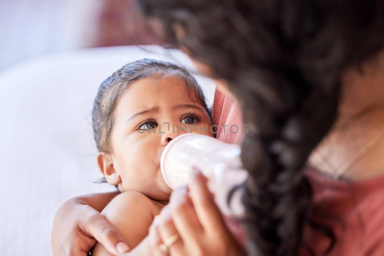 Hispanic mother feeding her little baby girl a bottle of milk formula. Tiny baby and mother bonding in the nursery together while drinking a bottle of milk. Mother holding her baby in the bedroom.