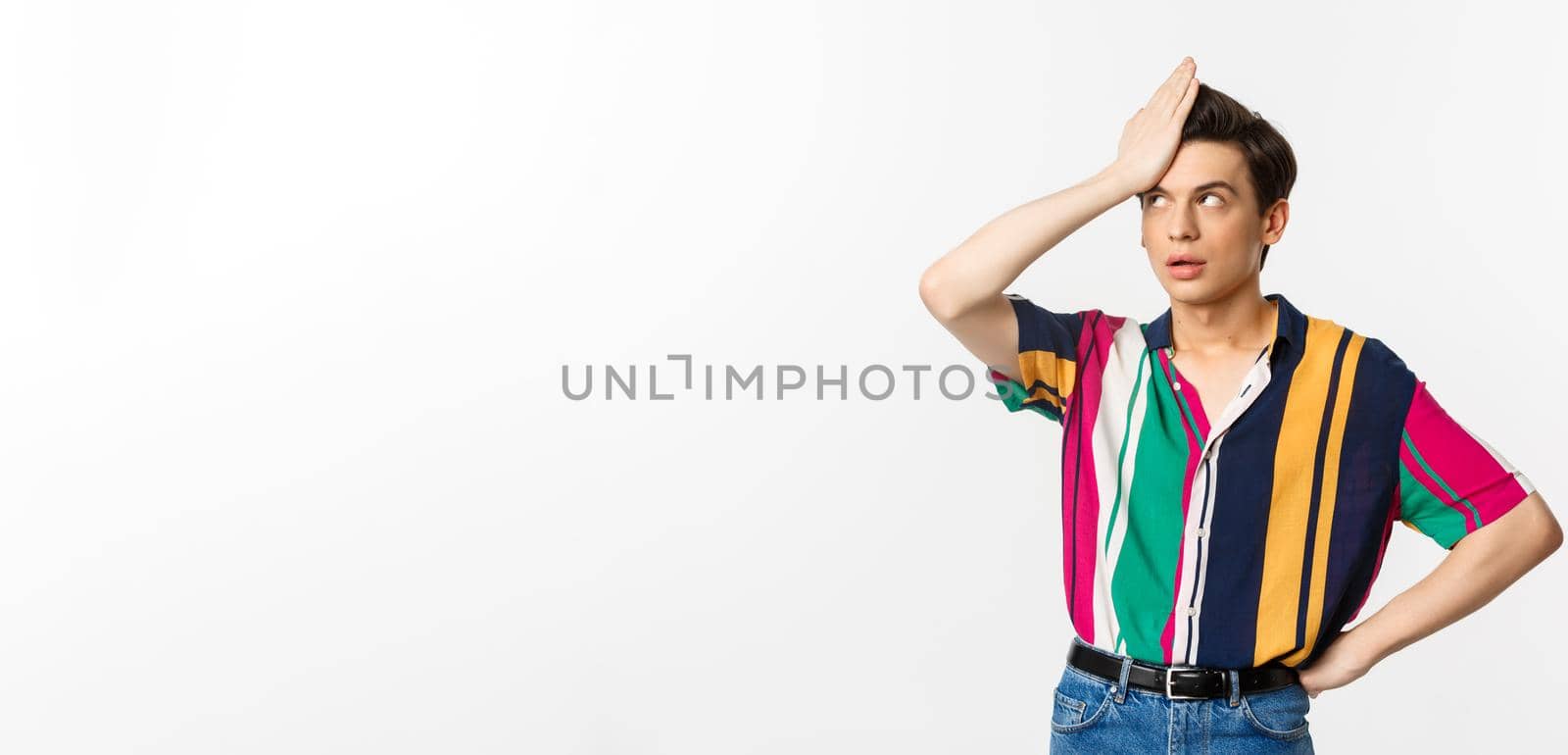 Annoyed gay man facepalm and roll eyes, standing disappointed and tired over white background.