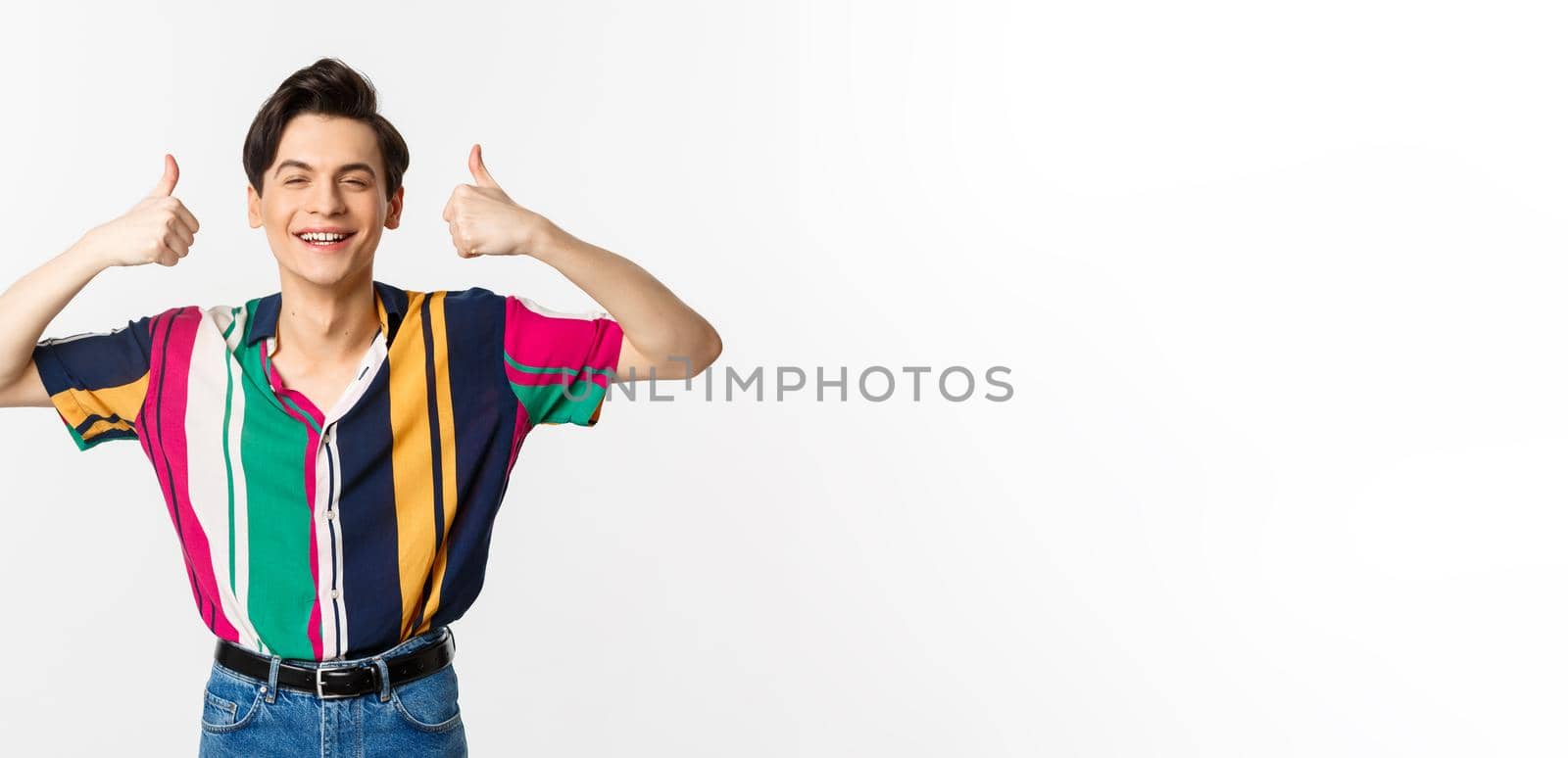 Young cheerful man smiling, showing thumbs up in approval, praise something good, standing over white background by Benzoix