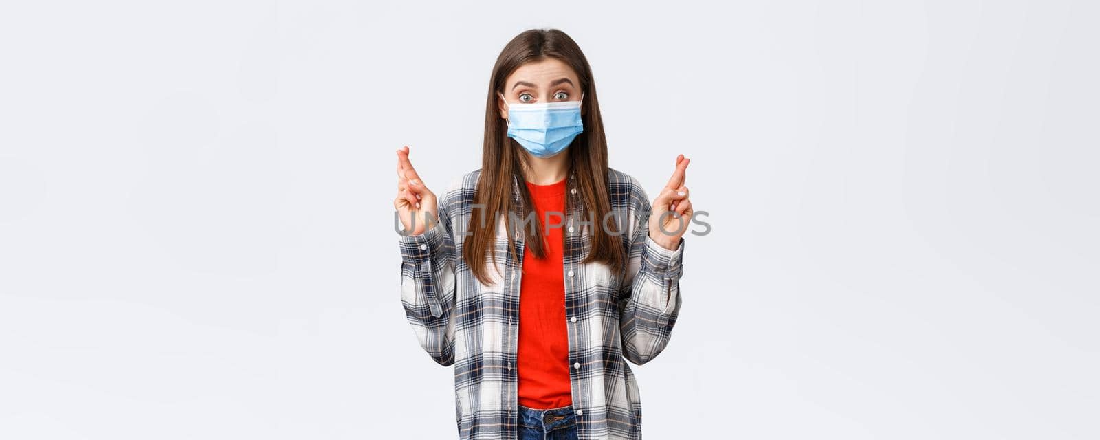 Coronavirus outbreak, leisure on quarantine, social distancing and emotions concept. Hopeful optimistic cute girl in medical mask have faith, cross fingers good luck, making wish or praying.