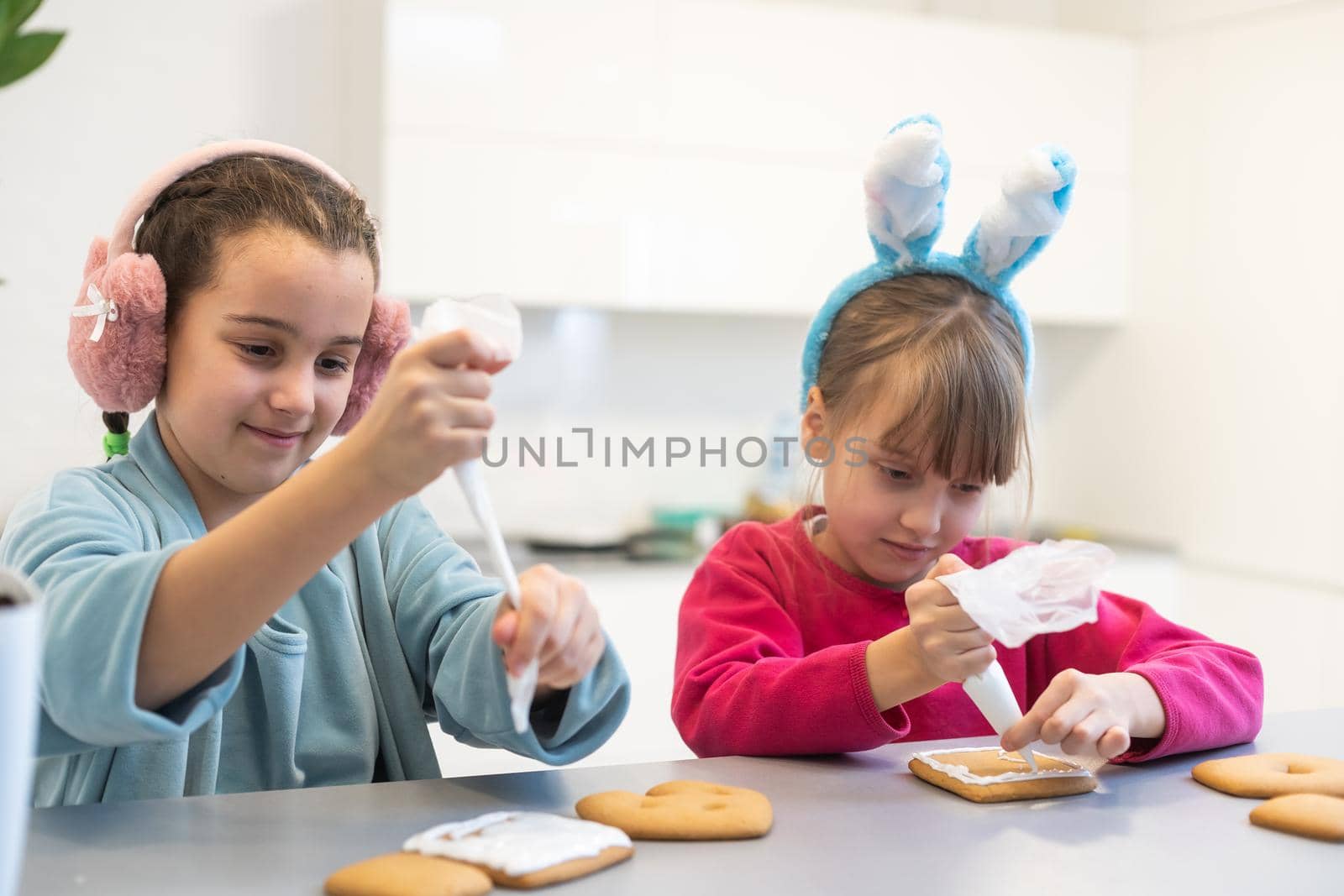 Two girls decorate cookies on plates with chocolate icing. Cooking treats for halloween celebration. Lifestyle by Andelov13