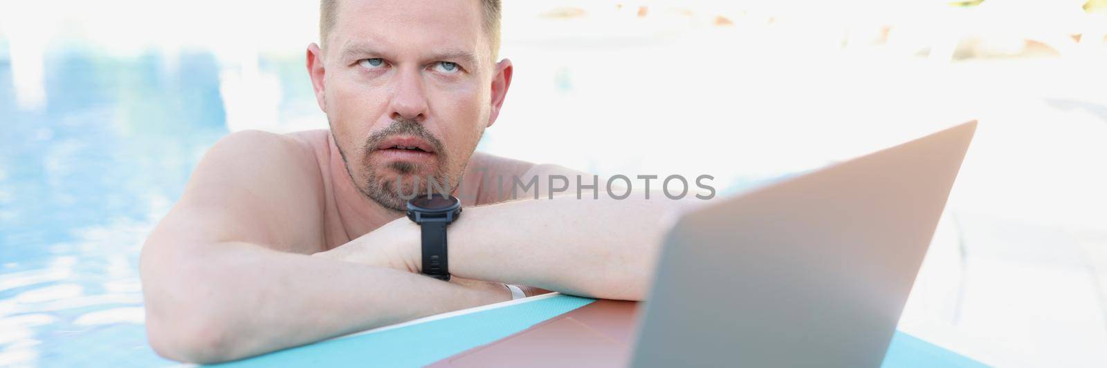 Annoyed man working on a laptop from the pool by kuprevich