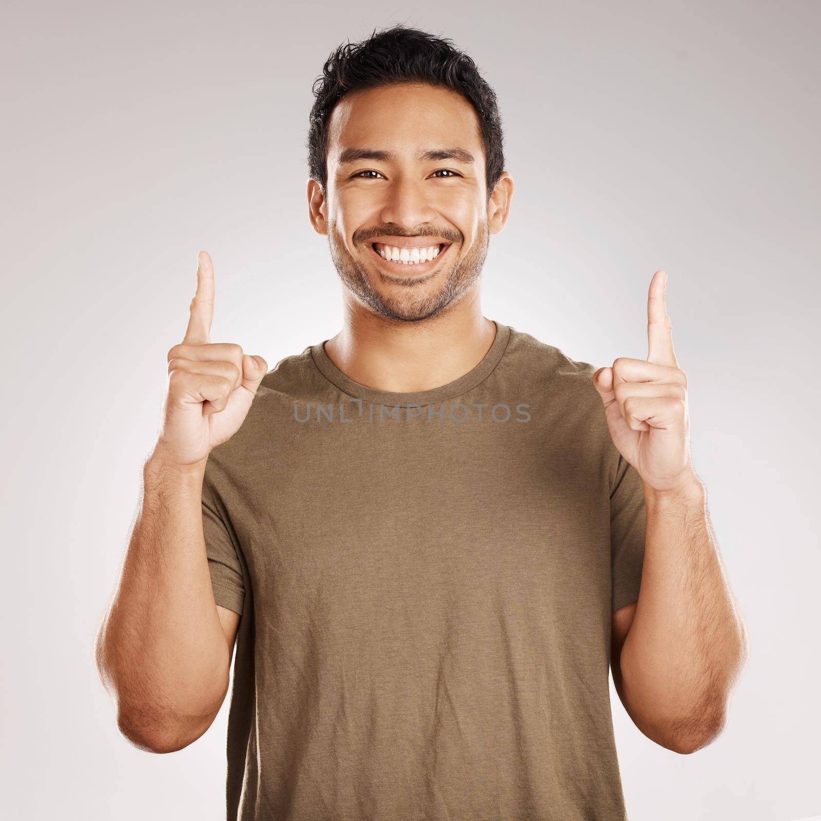 Handsome young mixed race man pointing towards copyspace while standing in studio isolated against a grey background. Happy hispanic male advertising or endorsing your product, company or idea by YuriArcurs