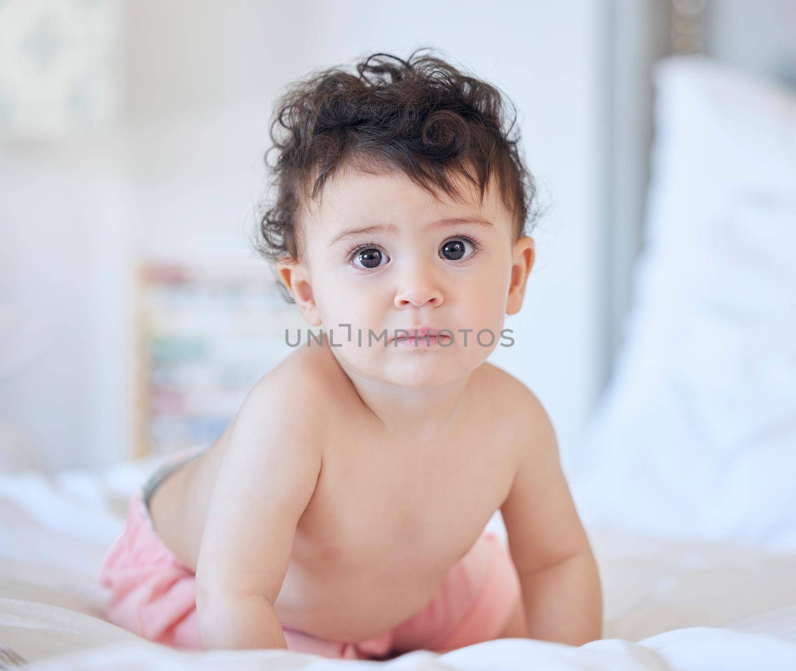 One caucasian baby girl playing alone on the bed at home in day or morning looking to the camera copyspace childhood and growing up concept.