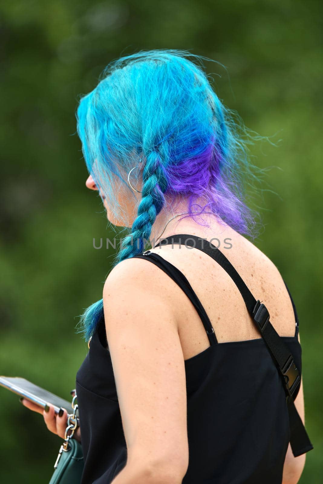 female with blue and lilac hair holds a phone in her hand. Bright color . punk girl, young woman with chic purple hair color with fluttering hair. Short hairstyle, fashion haircut. High quality photo