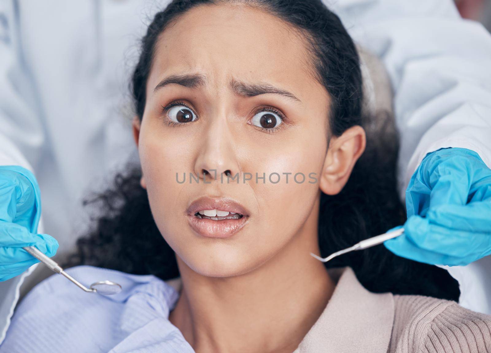 Oh no will this hurt. Shot of a young woman looking afraid at her dentists office. by YuriArcurs