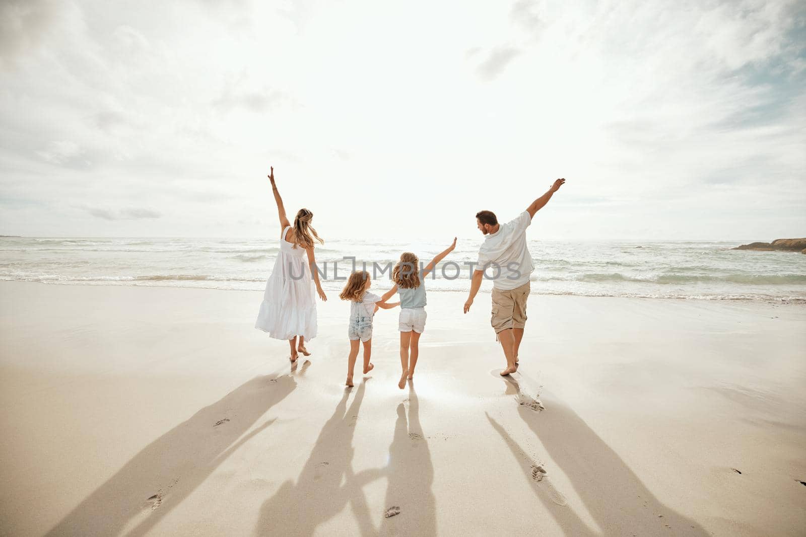 Back of happy caucasian parents with daughters enjoying free time on a beach. Little girls bonding with their mother and father and playing on weekend. Family pretending to fly with arms outstretched.