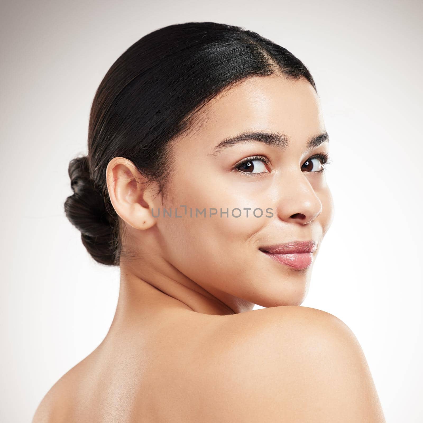 Face of a young beautiful mixed race woman smiling and posing against a grey studio background. Confident hispanic female posing against a background.