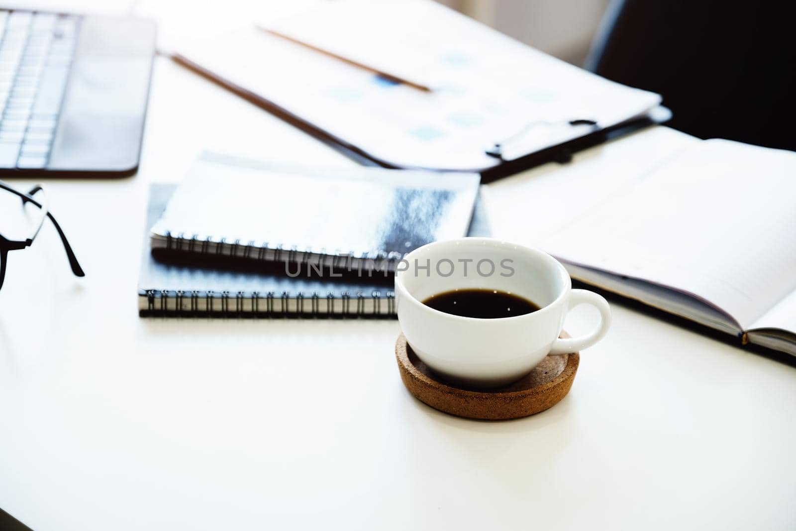 Focus on coffee mugs with books, documents with tablet computers on the desk by Manastrong