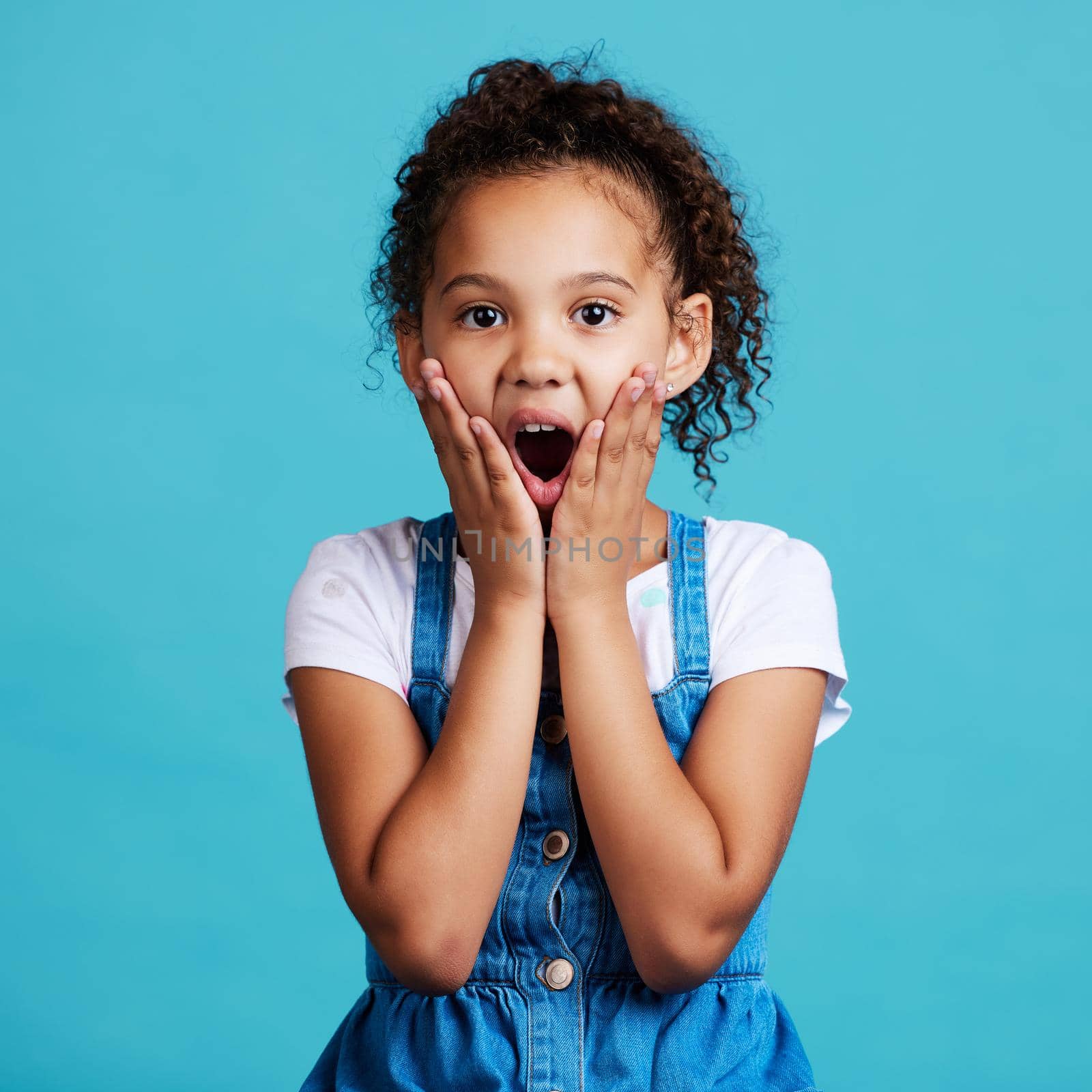 Shot of a little girl looking surprised while posing against a blue background.