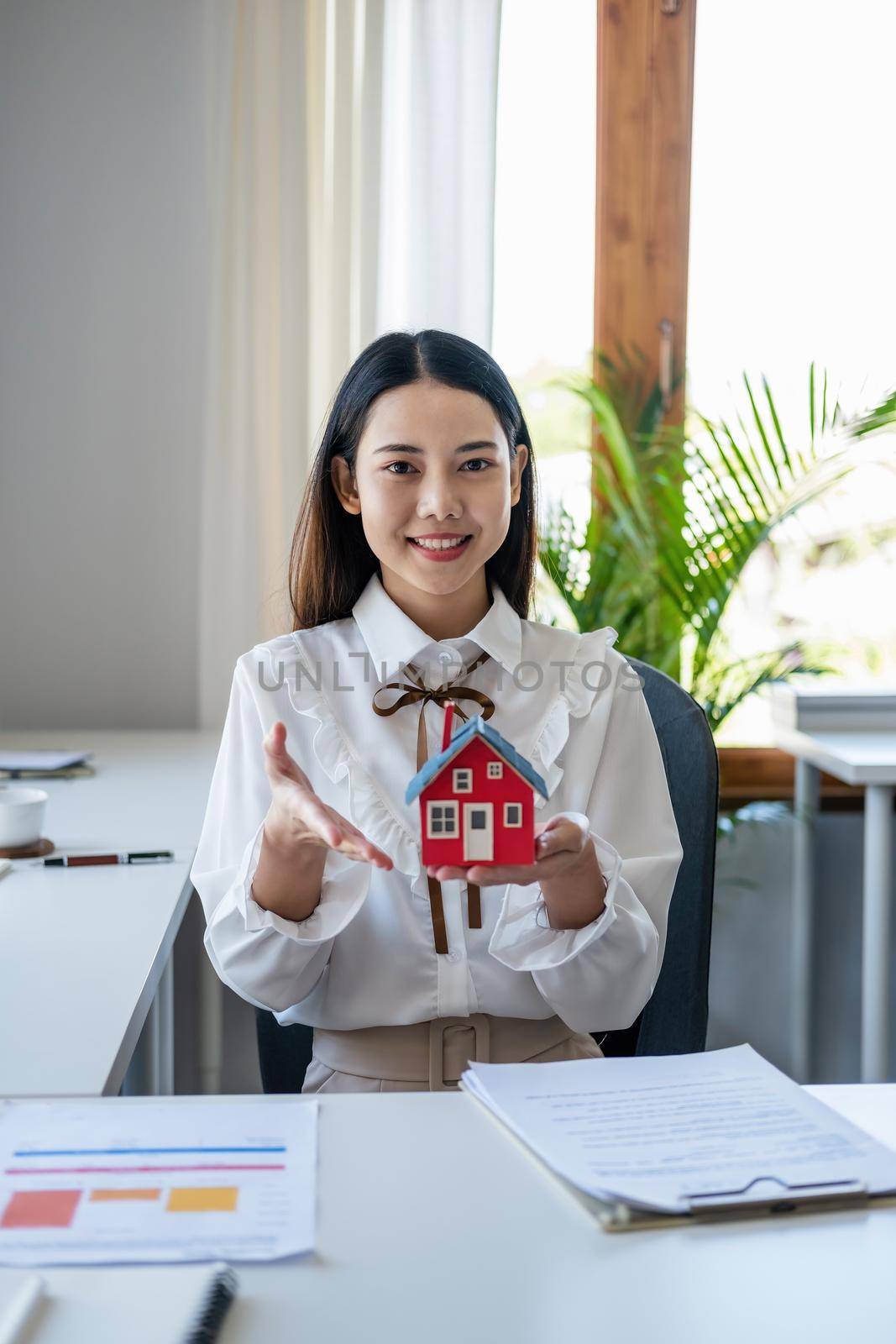 Accountant, businessman, real estate agent, Asian business woman handing model house to customers along with house interest calculation documents for customers to sign