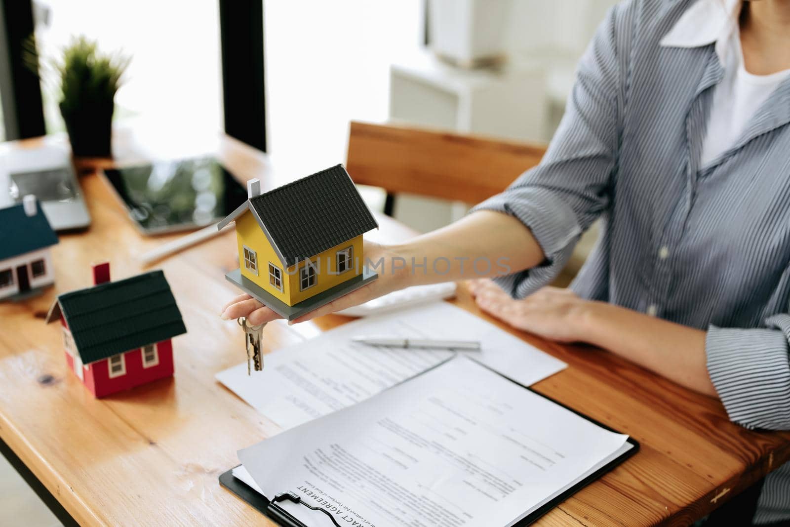 Accountant, businesswoman, real estate agent, Asian business woman handing model house and keys to customers along with house interest calculation documents for customers to sign.