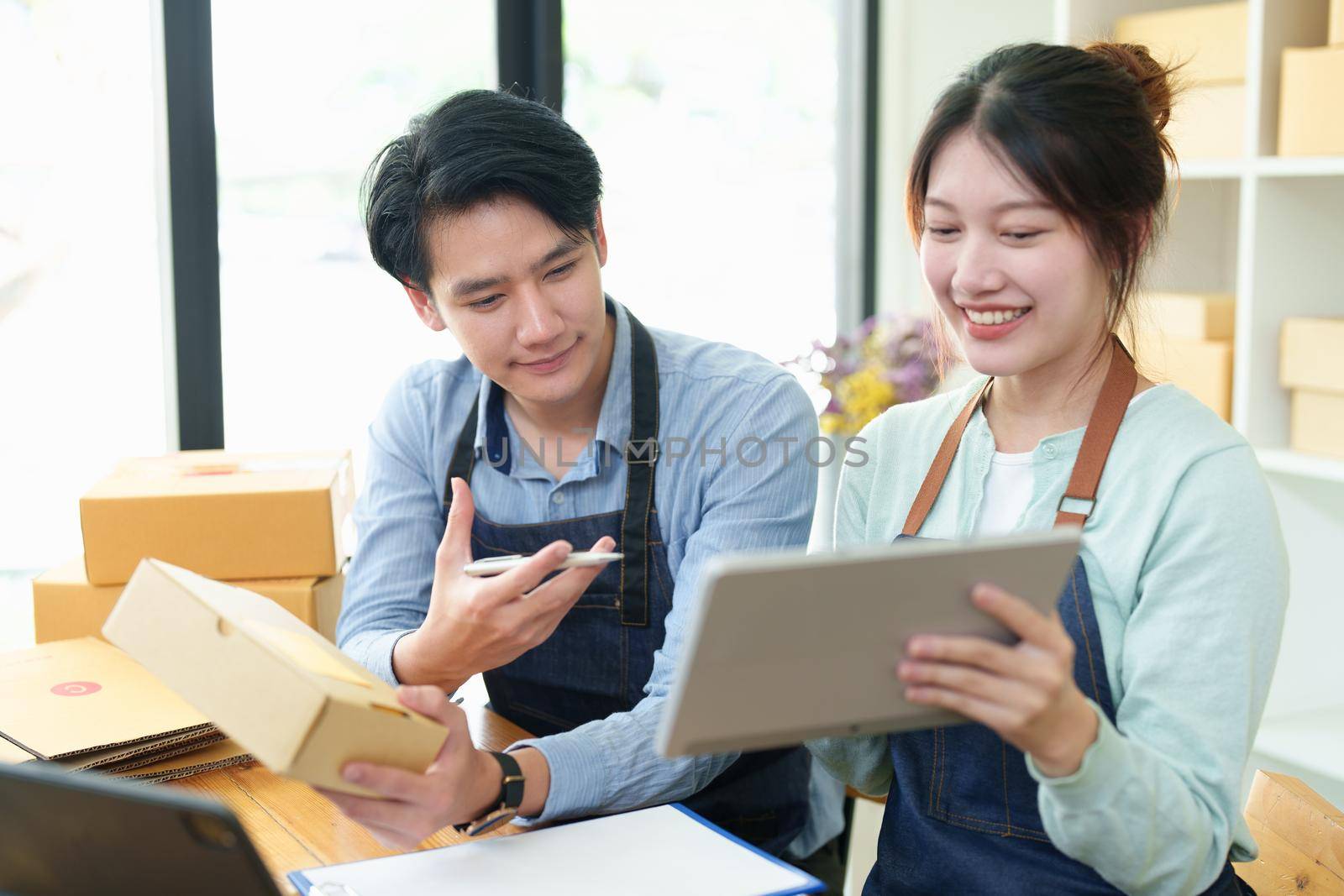 Portrait of a small start-up and SME owner, an Asian male and female entrepreneur checking orders and packing for customers, self-employed, freelance, online selling by Manastrong