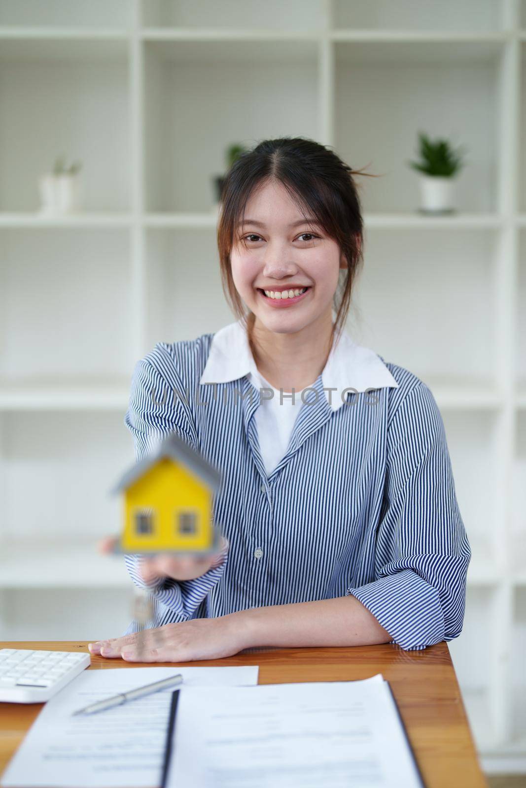 Accountant, businesswoman, real estate agent, Asian business woman handing model house and keys to customers along with house interest calculation documents for customers to sign by Manastrong