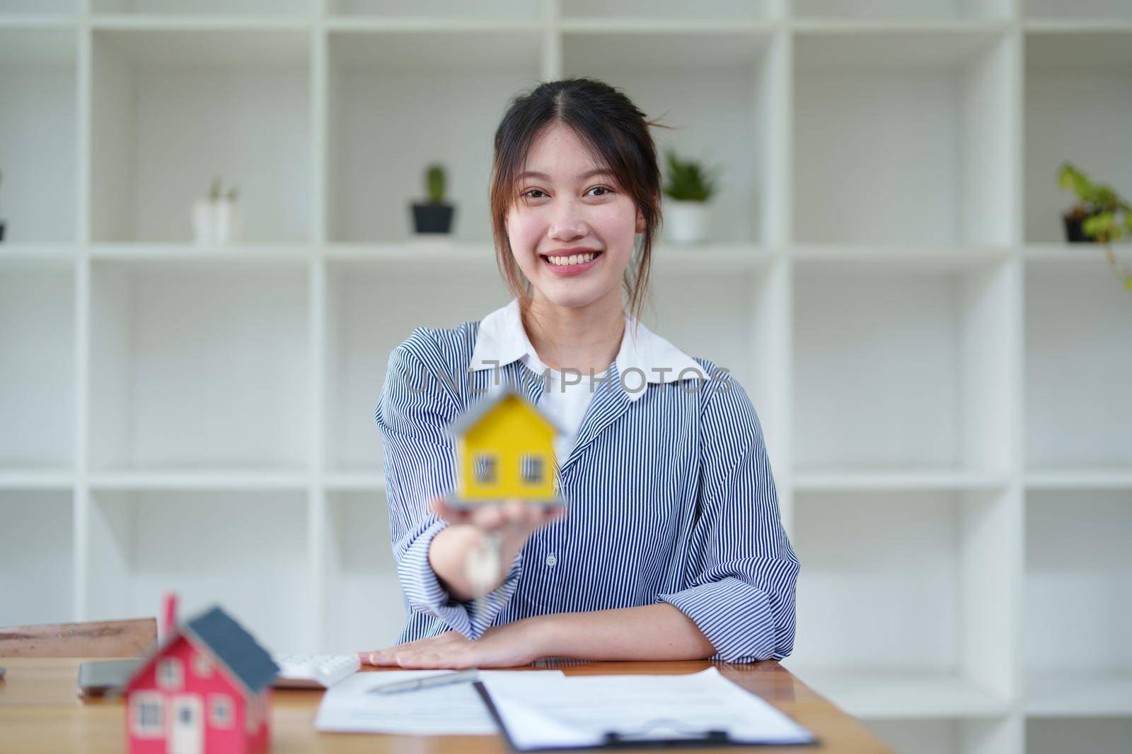 Accountant, businesswoman, real estate agent, Asian business woman handing model house and keys to customers along with house interest calculation documents for customers to sign.