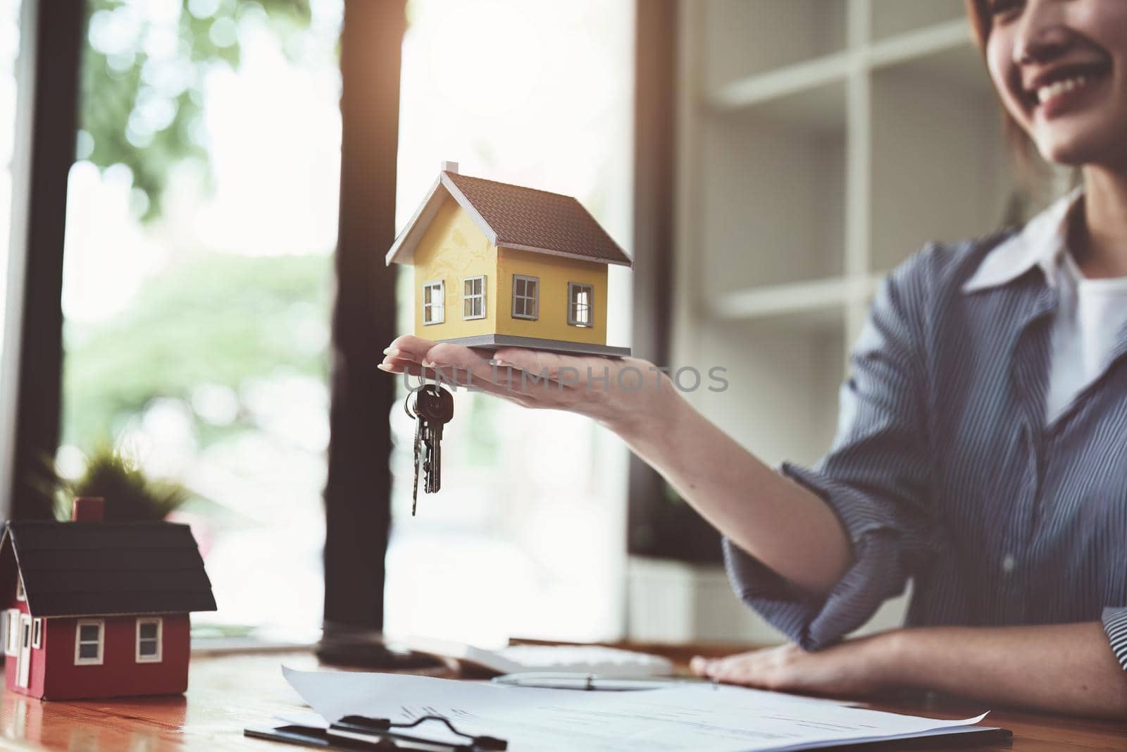 Accountant, businesswoman, real estate agent, Asian business woman handing model house and keys to customers along with house interest calculation documents for customers to sign.