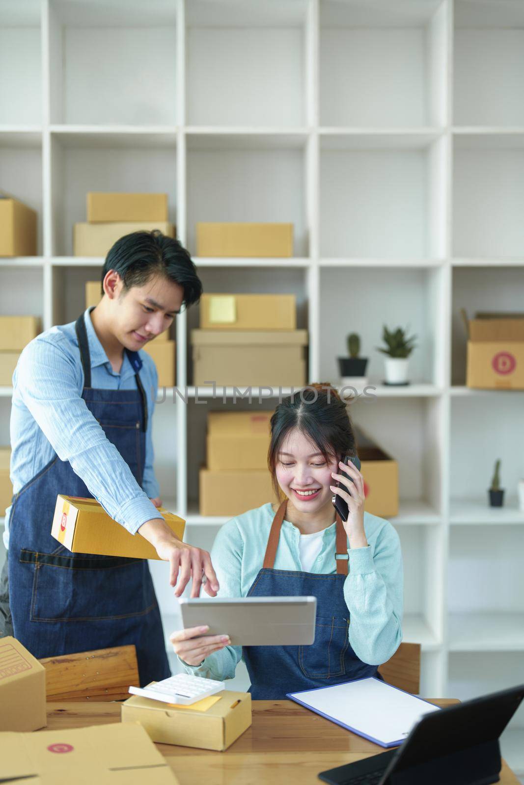 Portrait of a small start-up and SME owner, an Asian male and female entrepreneur checking orders and packing for customers, self-employed, freelance, online selling by Manastrong