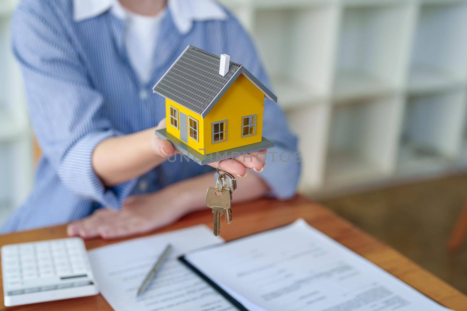 Accountant, businesswoman, real estate agent, Asian business woman handing model house and keys to customers along with house interest calculation documents for customers to sign.