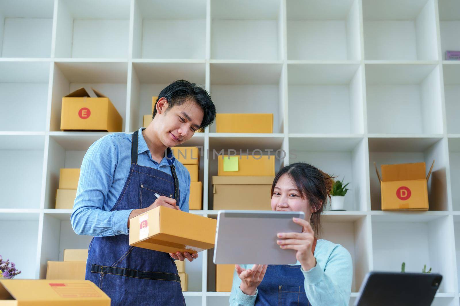 Portrait of a small start-up and SME owner, an Asian male and female entrepreneur checking orders and packing for customers, self-employed, freelance, online selling by Manastrong