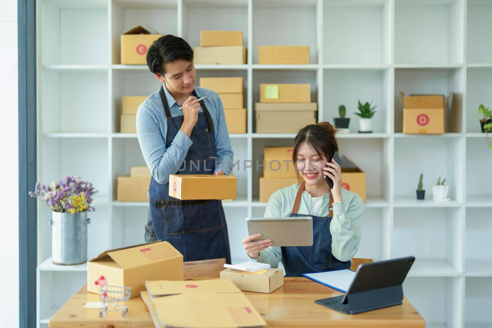 Portrait of a small start-up and SME owner, an Asian male and female entrepreneur checking orders and packing for customers, self-employed, freelance, online selling by Manastrong