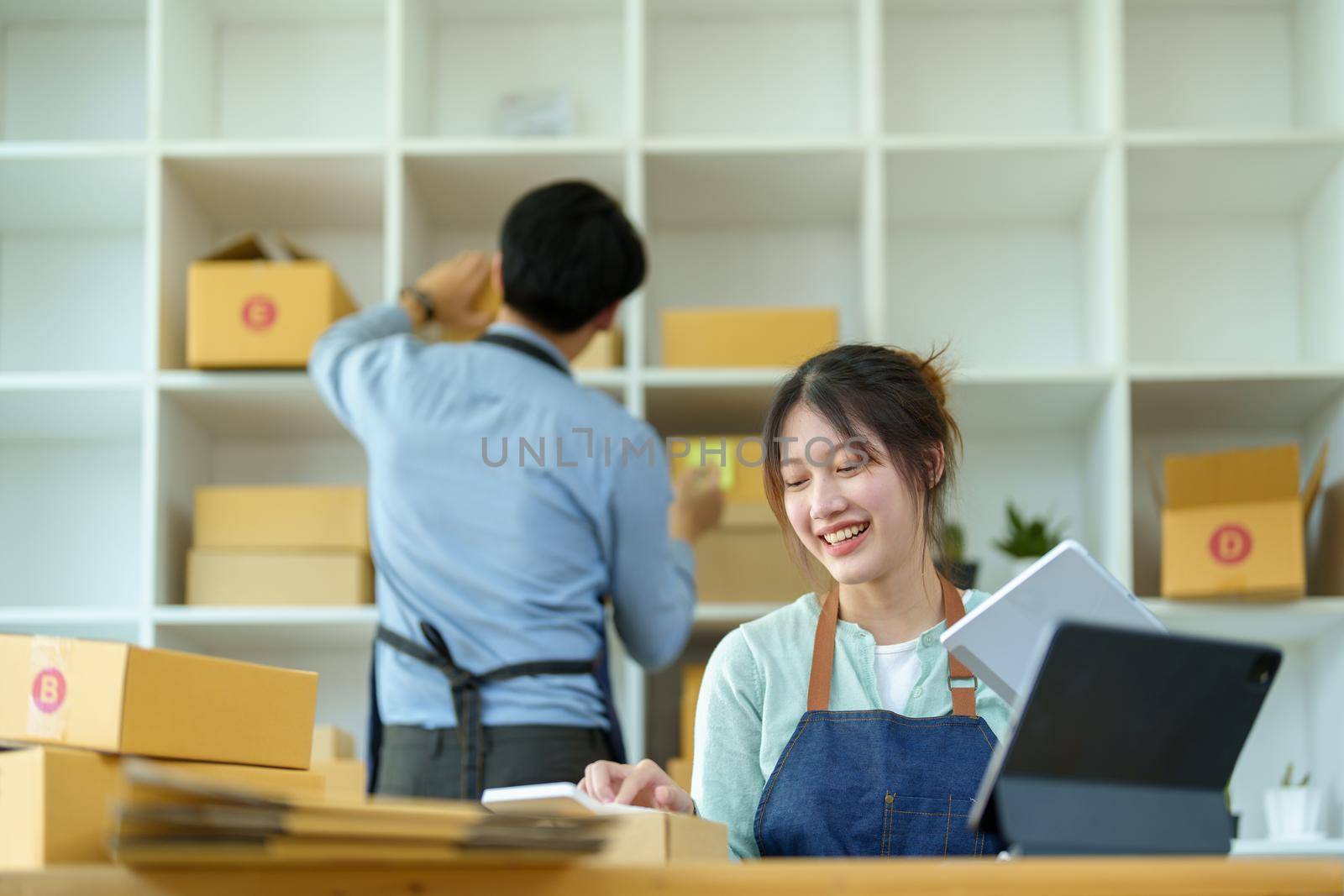 Portrait of a small start-up and SME owner, an Asian male and female entrepreneur checking orders and packing for customers, self-employed, freelance, online selling by Manastrong