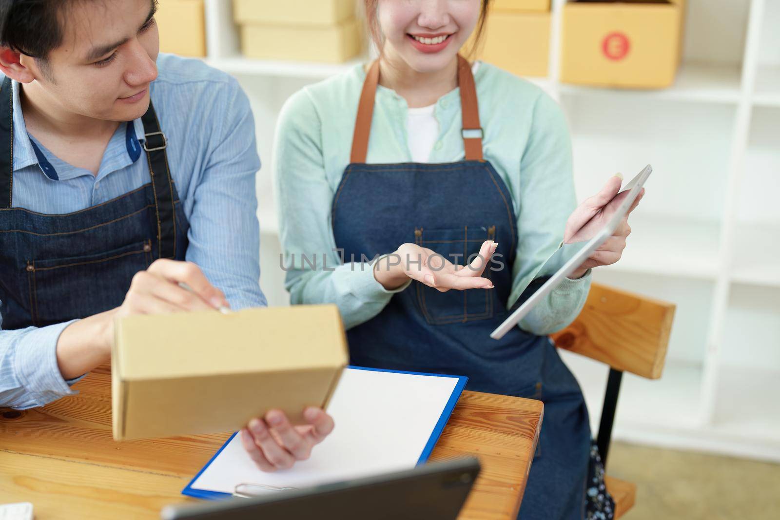 Portrait of a small start-up and SME owner, an Asian male and female entrepreneur checking orders and packing for customers, self-employed, freelance, online selling by Manastrong