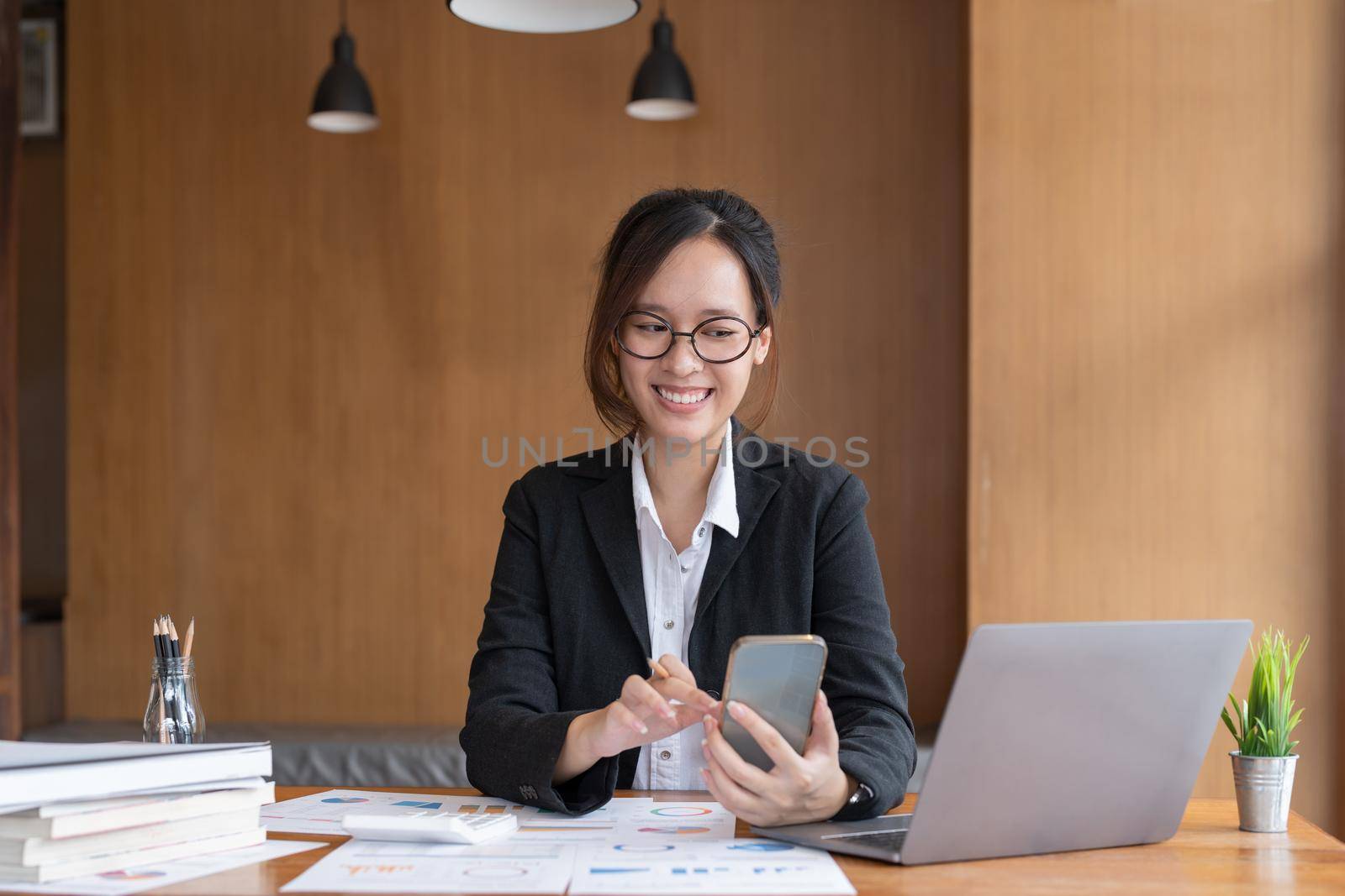Asian woman holding smart phone while using calculator for business financial accounting calculate money bank loan rent payments manage expenses finances taxes doing paperwork concept, close up. by nateemee