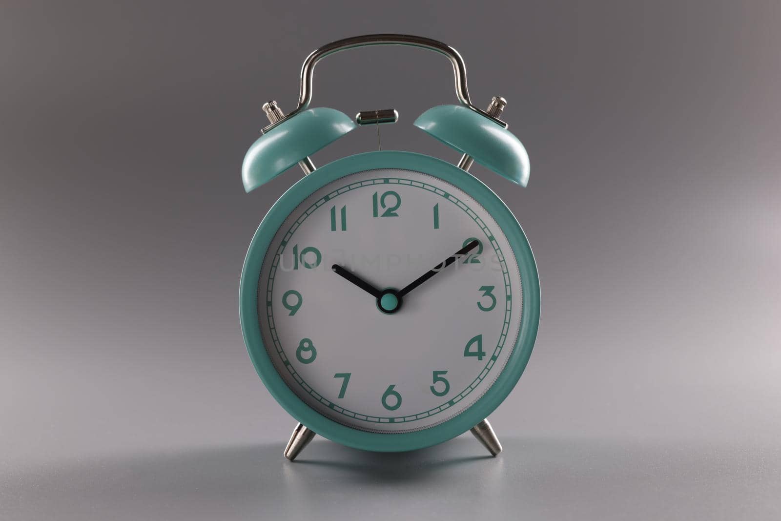 Close-up of single simple designed green retro clock on grey surface. Metal vintage clock on tiny legs stand. Time, timer, alarm, decor, rarity concept