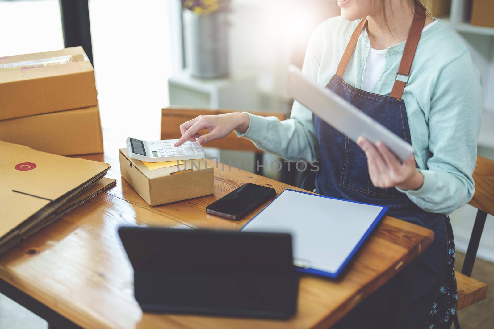 A portrait of .a small start-up and an SME owner, an Asian female entrepreneur using a calculator to calculate profits from selling products online by Manastrong