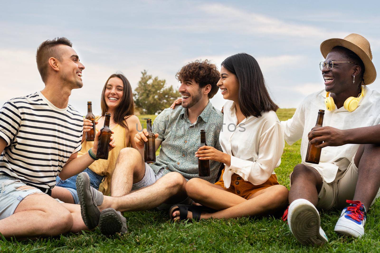 Multiracial friends laughing together enjoying some cool beer outdoors in park. Having fun. Friendship and community concepts.