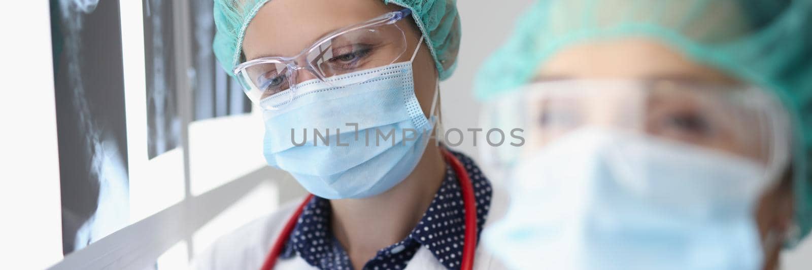 Portrait of women professional doctor look through x ray scans in hospital. Colleagues in protective uniform examine analysis. Diagnostic, medicine concept