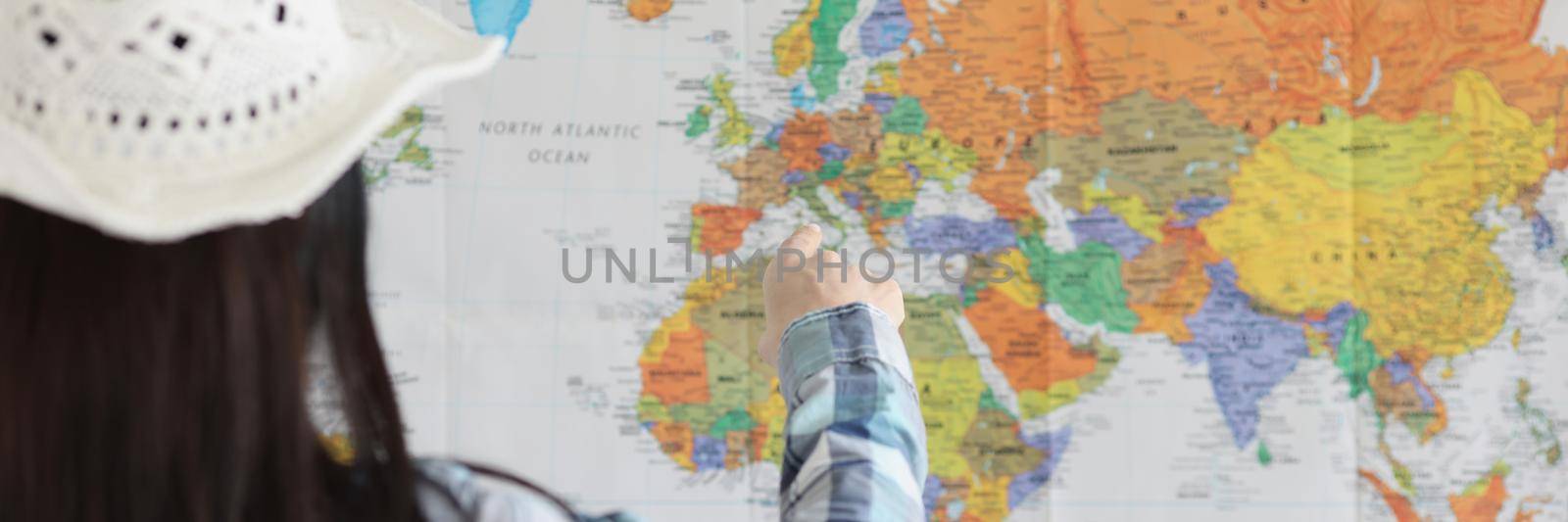 Close-up of woman point on world map with finger and decide what country to go next. Young female traveler explore world. Adventure, tourist, plan concept