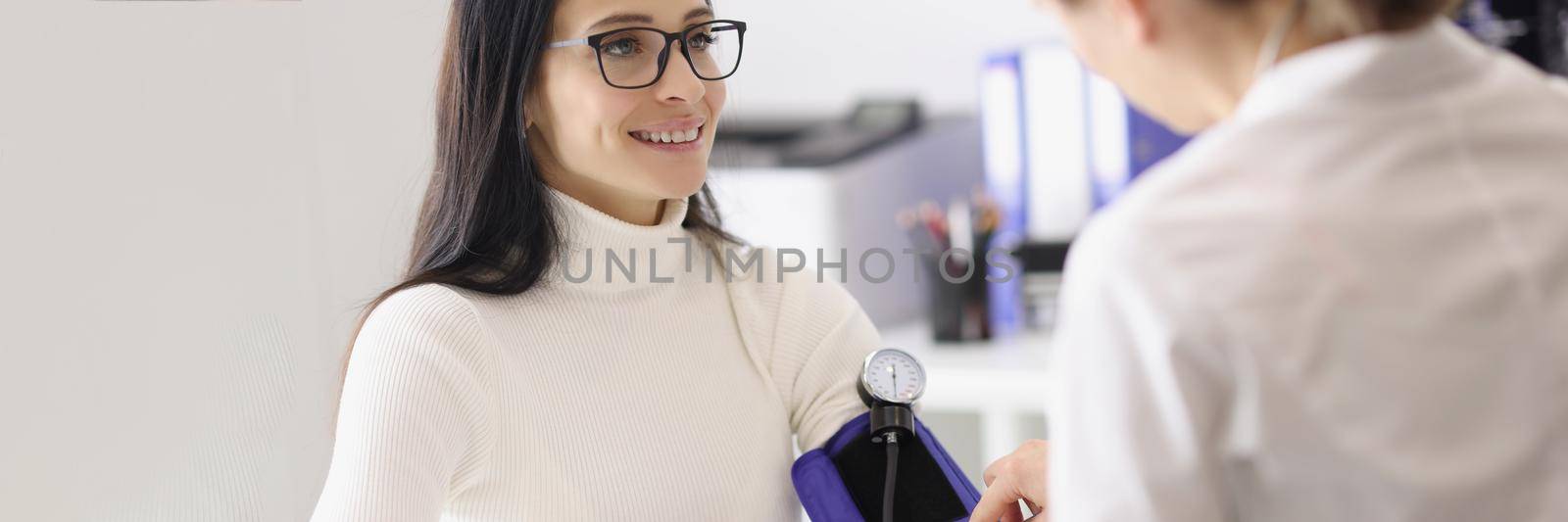 Portrait of doctor measuring patients blood pressure with tonometer tool and talk. Planned checkup at family doctor. Medicine, healthcare, clinic concept
