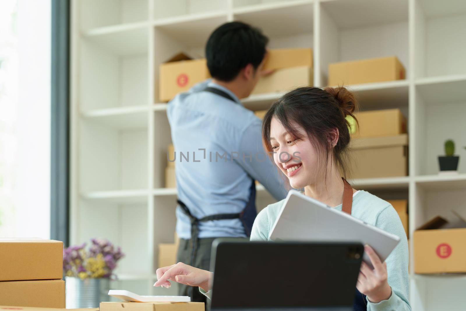 Portrait of a small start-up and SME owner, an Asian male and female entrepreneur checking orders and packing for customers, self-employed, freelance, online selling by Manastrong