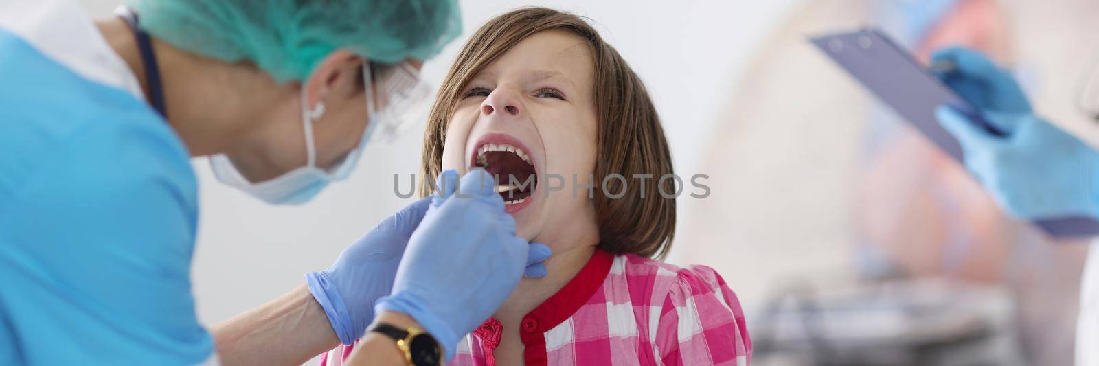 Portrait of little child open mouth for check up, hurting throat, pediatrician appointment check with tool. Young female doctor examine. Medicine concept