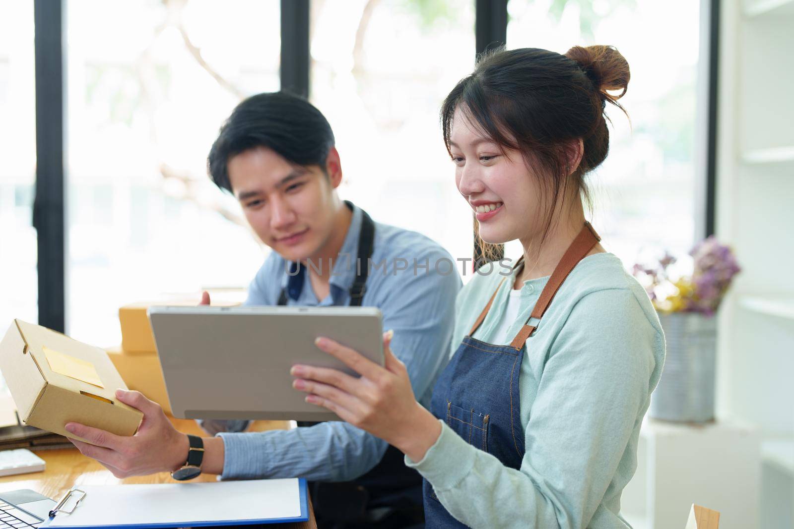 Portrait of a small start-up and SME owner, an Asian male and female entrepreneur checking orders and packing for customers, self-employed, freelance, online selling by Manastrong