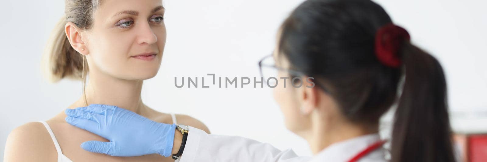 Portrait of blonde female on doctors appointment being examined by professional medical worker. Nurse touch neck and chest. Provide help, health concept