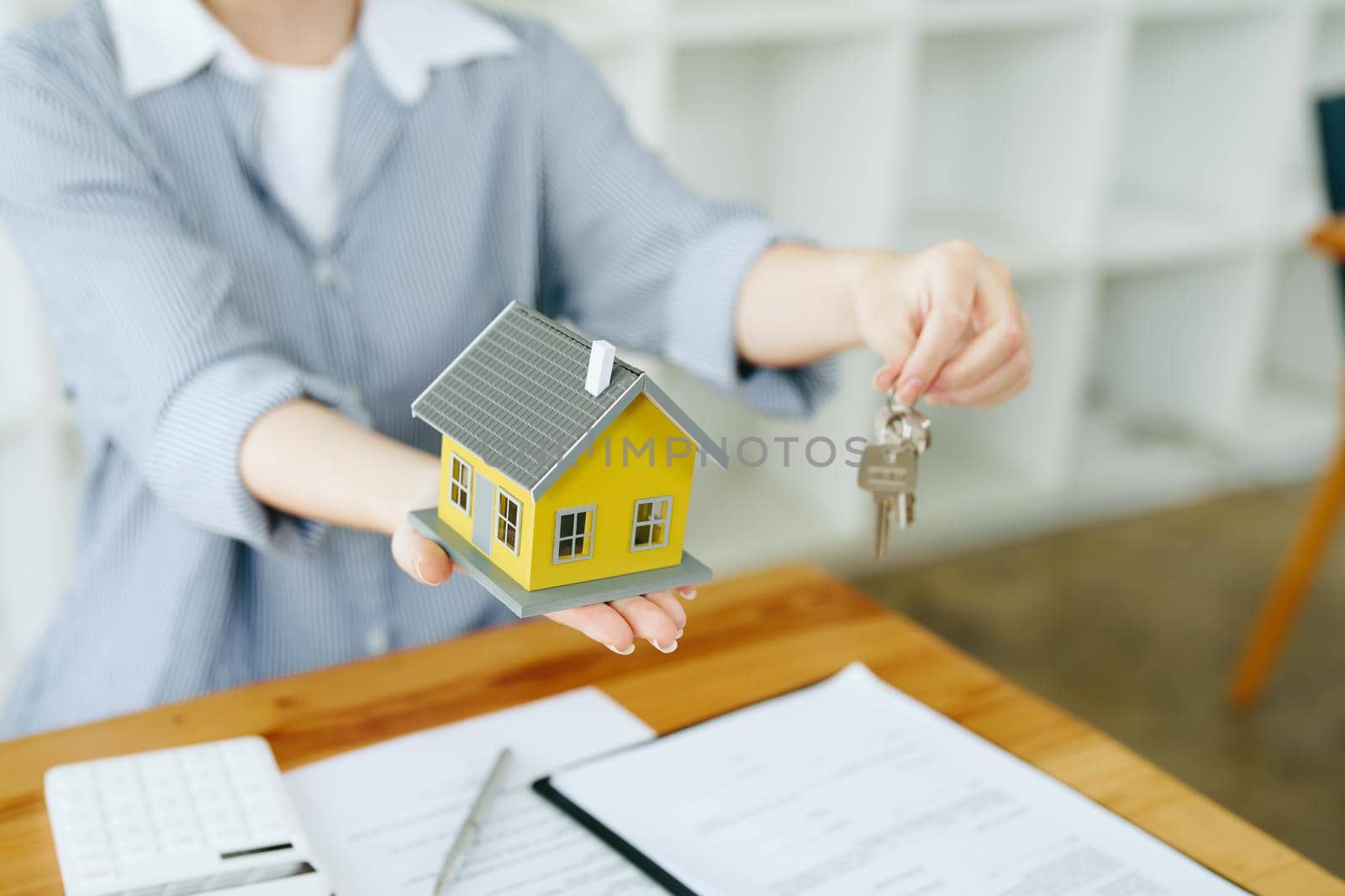 Accountant, businesswoman, real estate agent, Asian business woman handing model house and keys to customers along with house interest calculation documents for customers to sign.