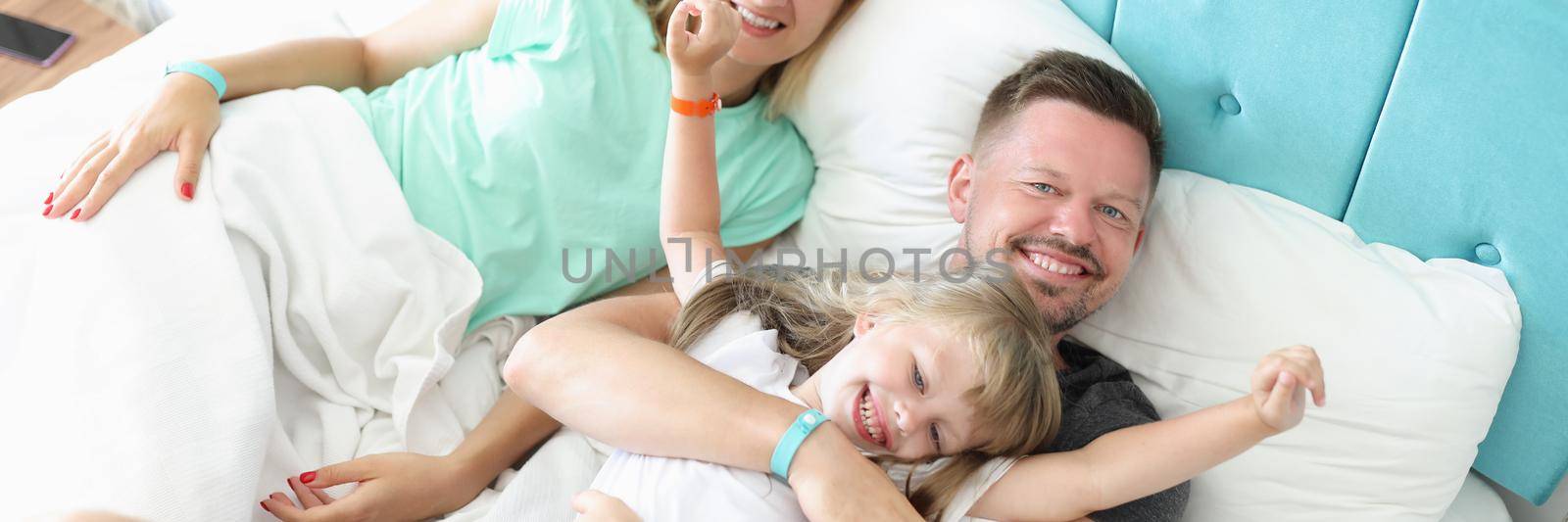 Lovely family rest in bed, father mother and daughter hug in morning by kuprevich