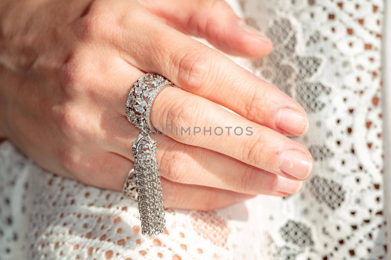 Close up of beautiful tribal boho style woman hands with lots of accessories. Boho style for fashionable look on resort. Middle aged well looking woman in white dress and boho style braclets. by panophotograph