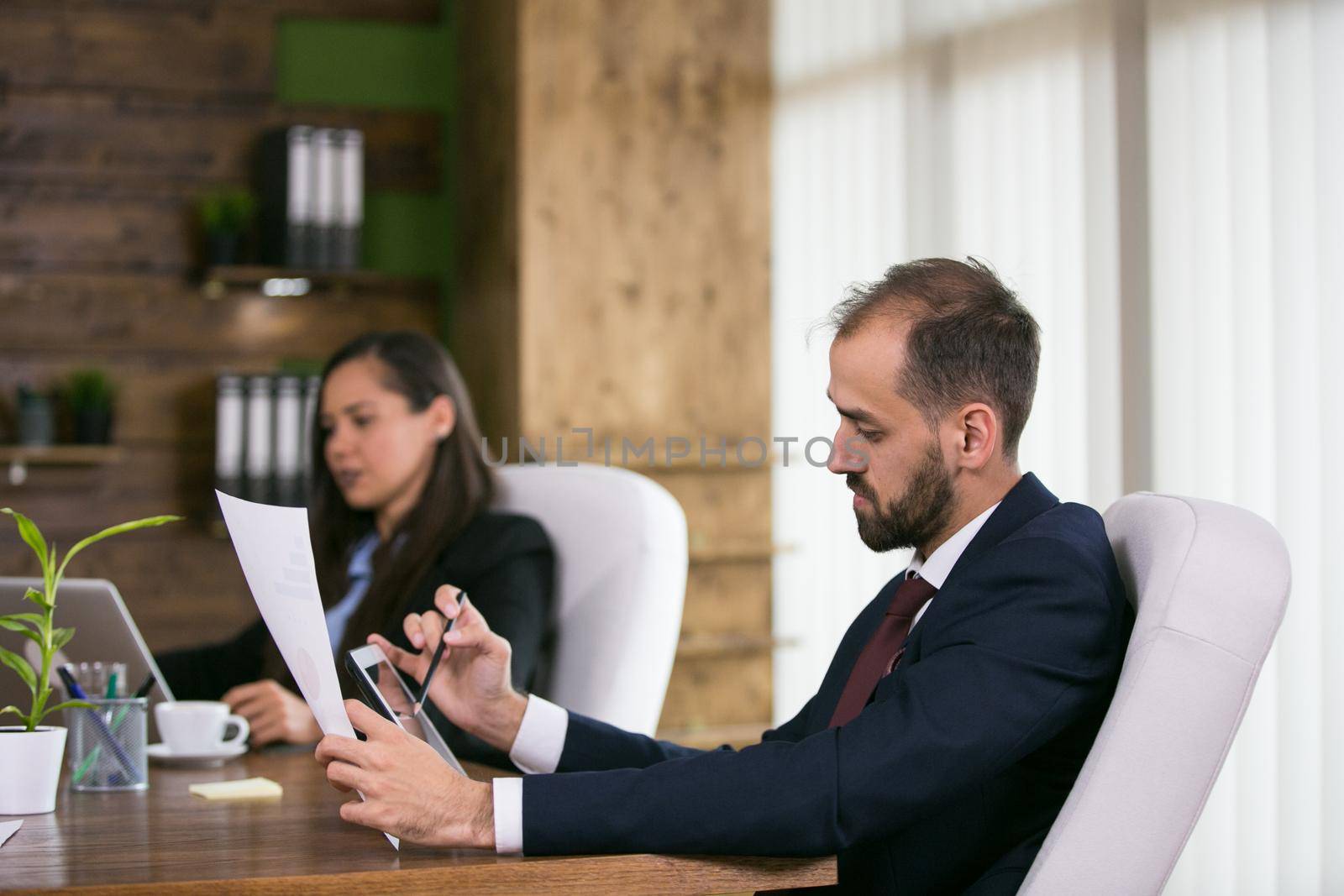 Businessman in suit in a conference room working on tablet by DCStudio
