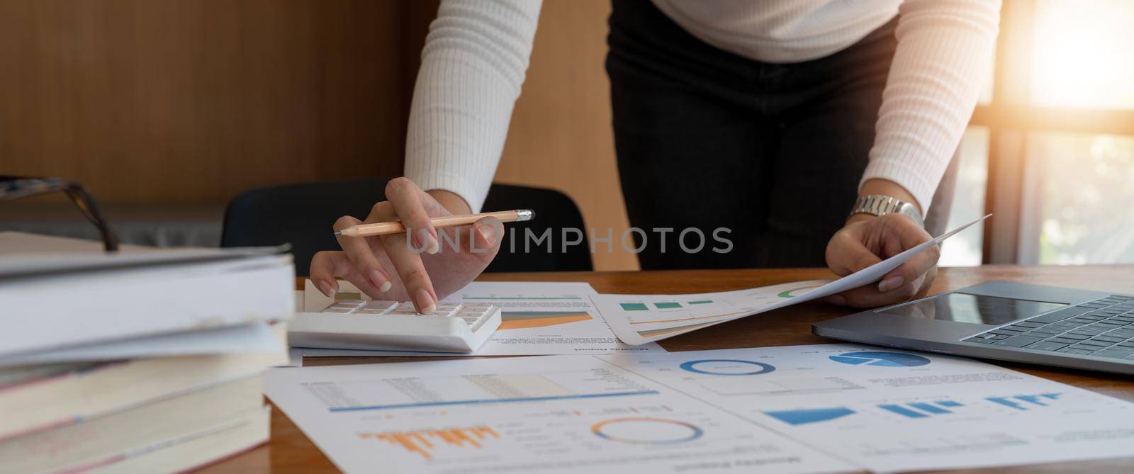 Close up of businesswoman or accountant working on calculator to calculate business financial data, accountancy document and laptop computer at office, business concept by nateemee