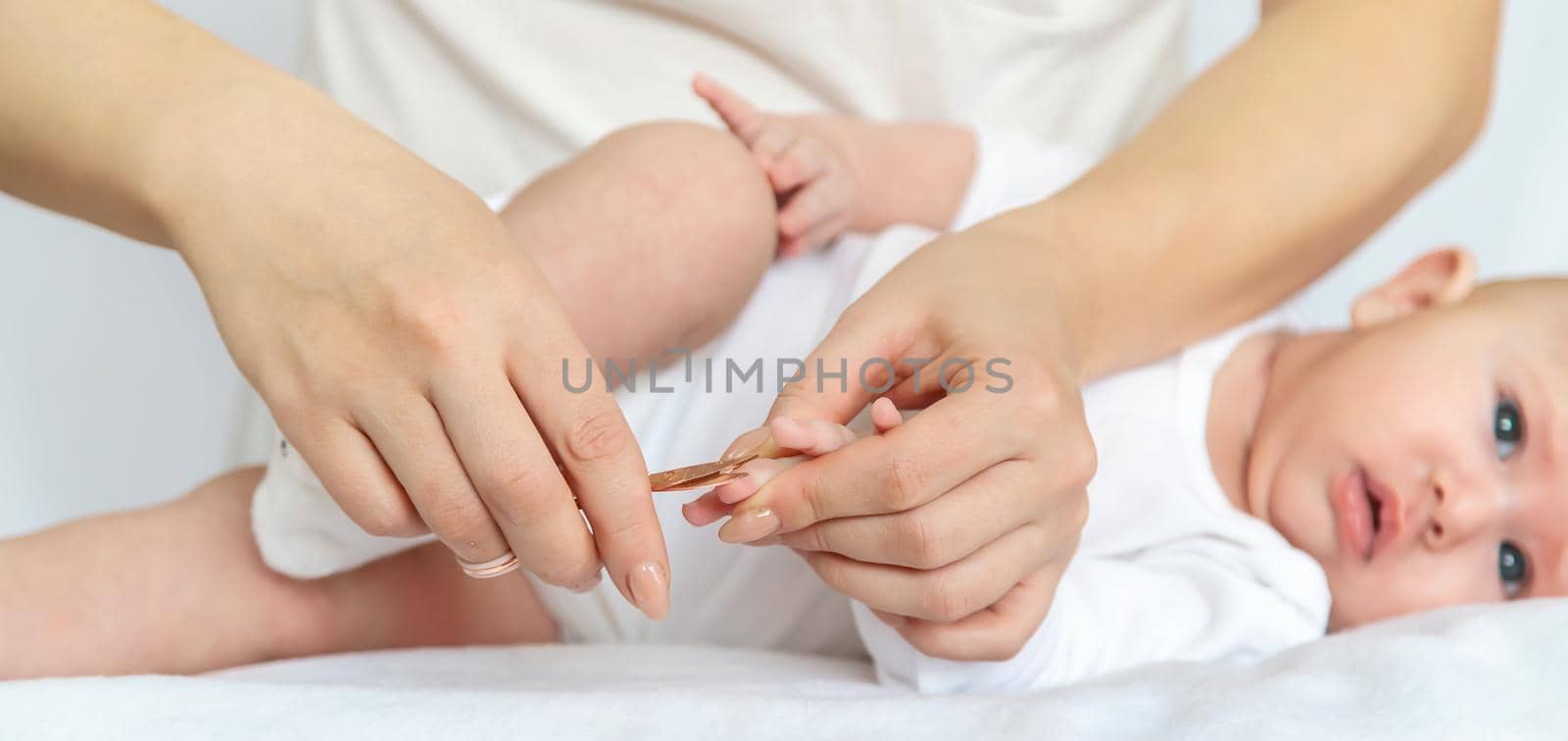 Mother cuts baby's fingernails on light background. Selective focus. people.